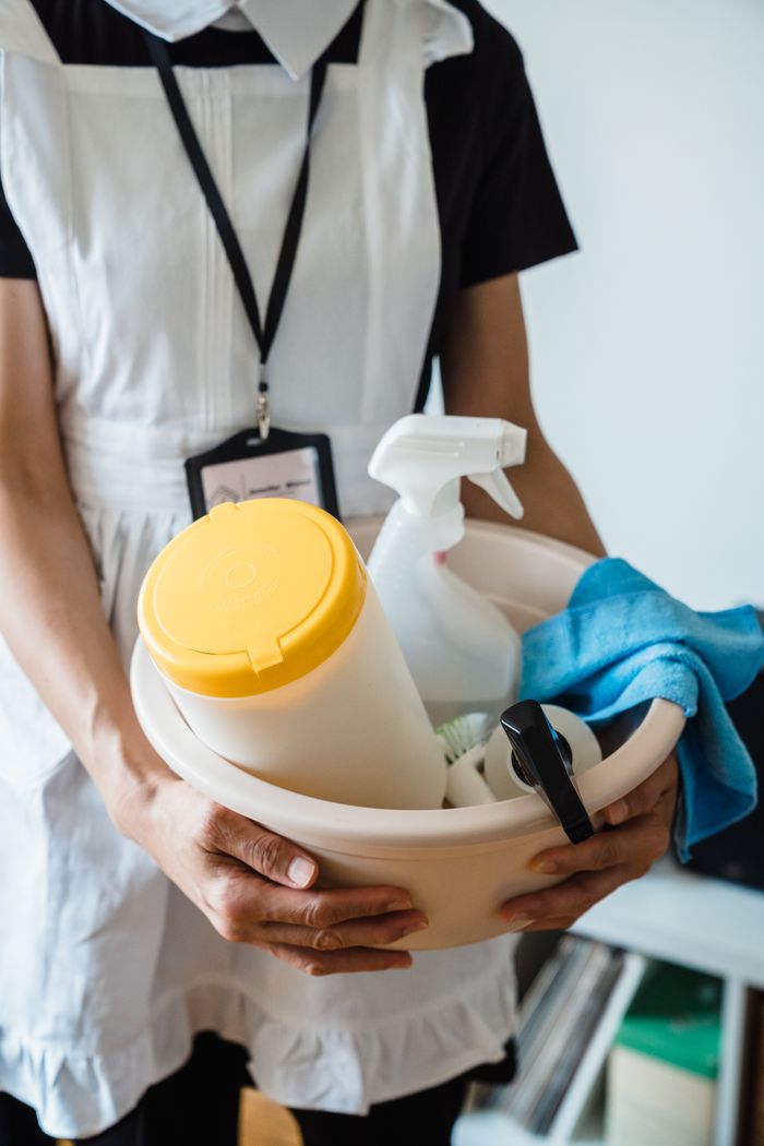 hero-01 A uniformed cleaner holding a basin with cleaning supplies indoors. Ideal for cleaning and sanitation themes.